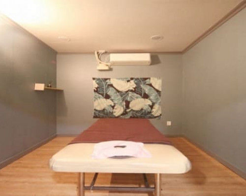 상인동 타이n테라피 1인실, 중앙에 마사지 베드가 보이며 1회용 해면과 깔끔한 타월이 깔려있다, 벽에는 휴양지 느낌의 초록색 장식과 에어컨이 걸려있음