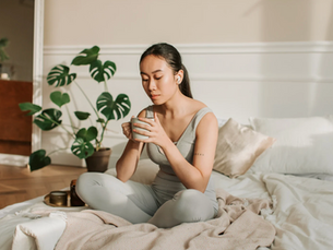 Women sat on her bed drinking a hot drink.