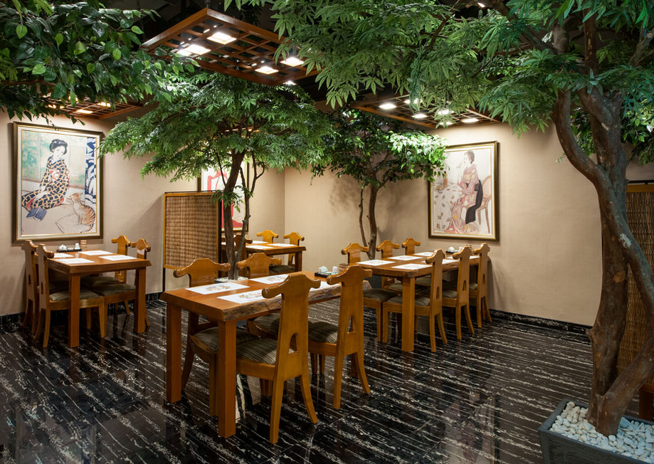 Warmly lit Japanese restaurant interior featuring wooden tables, unique chairs, indoor trees, and traditional wall art.