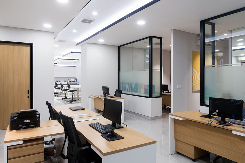 Modern open-plan office featuring wooden desks with computers, black task chairs, and glass-paneled meeting rooms.