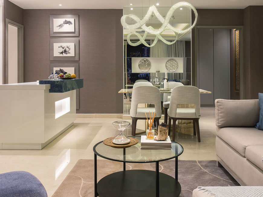 Architectural view of a modern apartment interior showcasing a custom TV feature wall, open-plan kitchen layout, and statement ceiling lighting.
