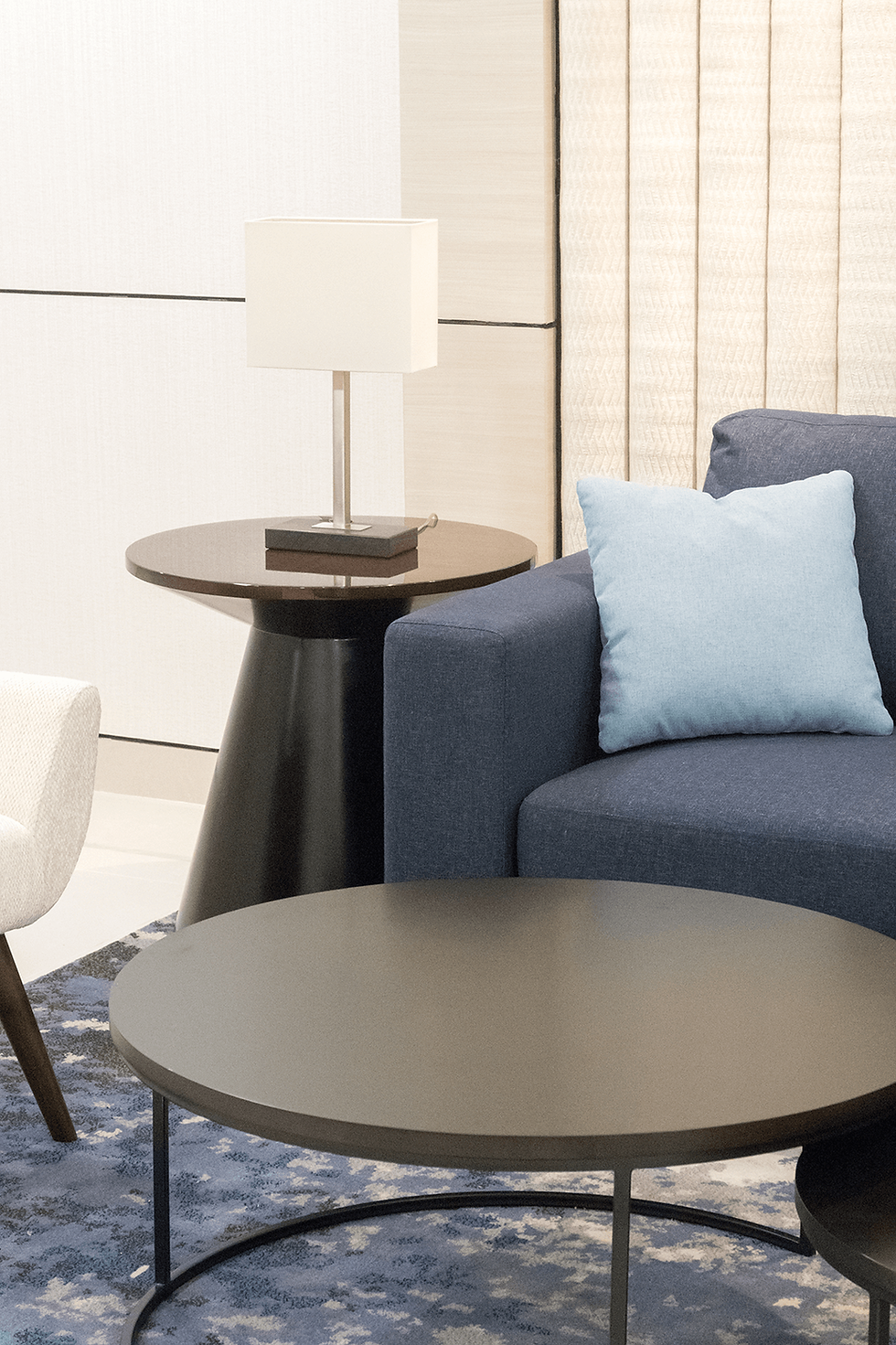 Close-up of a navy blue sofa with a light blue cushion next to a round side table with a modern lamp.