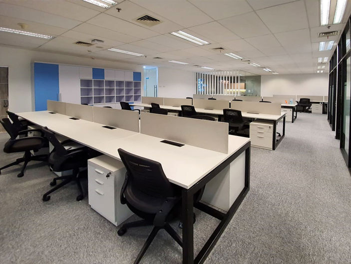 Wide view of a modern open office layout featuring rows of white desks with low dividers, black rolling chairs, white filing cabinets, and grey carpeting.