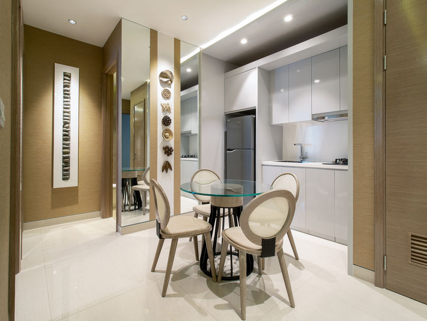 Apartment dining area with a round glass table and four chairs beside a modern white kitchenette, featuring tan textured wallpaper, decorative wall art, and a large mirror panel.