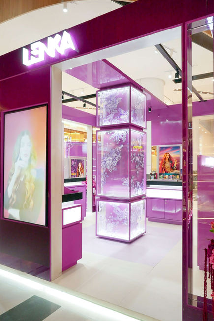 Entrance to a purple LENKA beauty store featuring a tall illuminated display tower with etched floral graphics and a large beauty portrait lightbox.