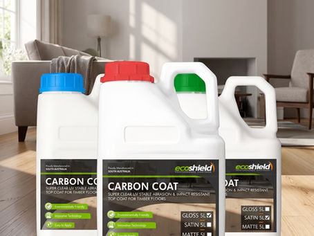 Three white 5-litre plastic bottles of Ecoshield Carbon Coat for Timber standing on a polished natural wood floor inside a modern living room. The bottles display labels showcasing Gloss, Satin, and Matte finishes with distinct red, green, and blue caps, casting soft reflections onto the clean timber surface.
