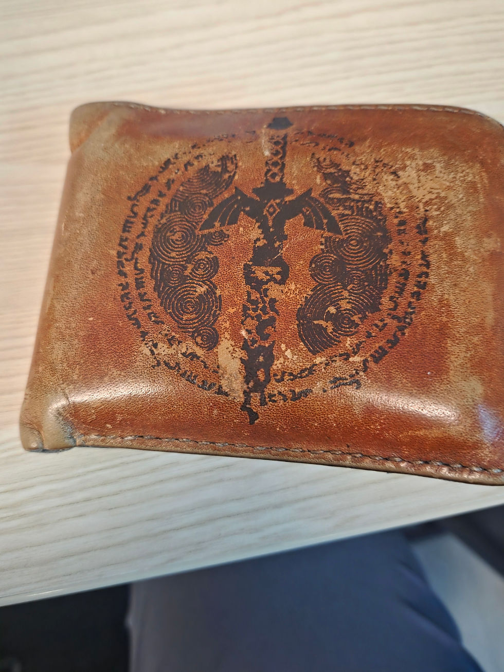A worn, brown leather wallet with the image of a degraded sword