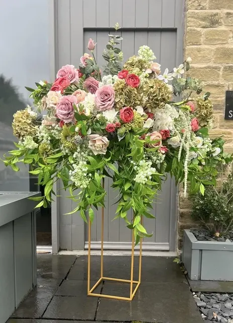 Luxurious floral arrangement featuring high-quality artificial roses, hydrangeas, and lush greenery on a modern gold stand, ideal for weddings, events, and venue styling in the UK