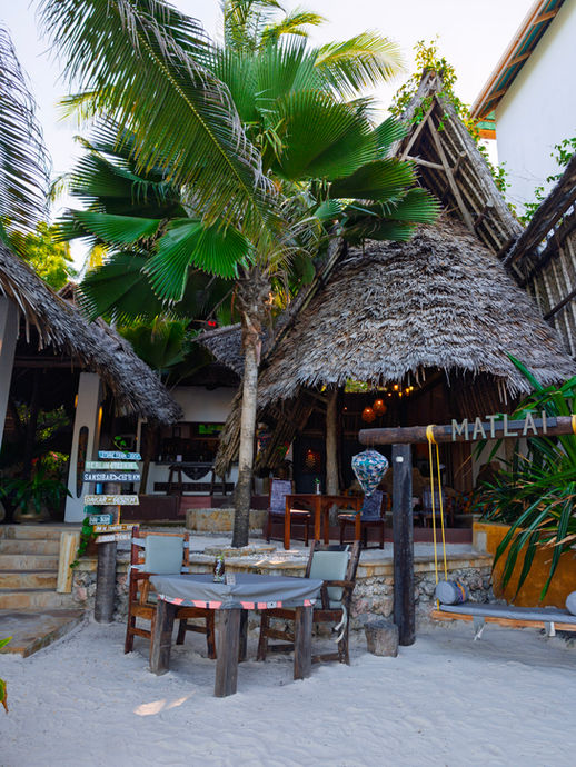 Beach bar entrance at Boutique Hotel Matlai Zanzibar with a large swing and dhow boat dining table overlooking the beach.