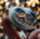 Luxury gold skeleton watch with exposed mechanical movement and polished case – held in hand against blurred light