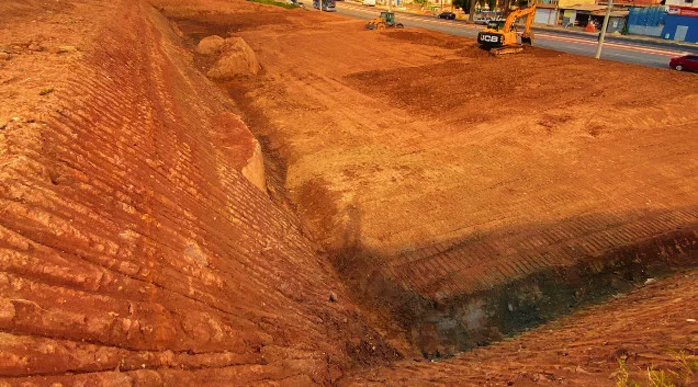Terraplanagem com corte de talude em 45º e escavadeira em ação na obra em Sinop, destacando a execução dos serviços de topografia.