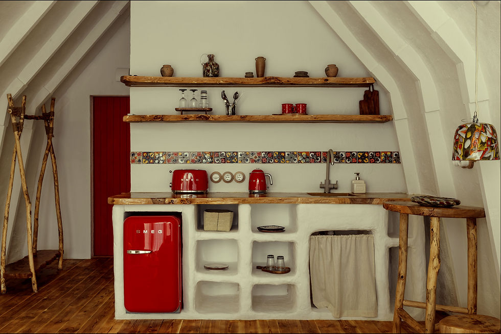 Rustic kitchen with a red SMEG fridge, red toaster and kettle. Wooden shelves hold pottery. Colorful tile accent and natural wood elements.