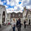 Thumbnail: People stroll along a cobblestone street in a historic town. Two women in the foreground are pointing at something.