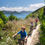 Thumbnail: Three people are biking on a narrow dirt path surrounded by lush greenery, enjoying a scenic trail with views of the sea.
