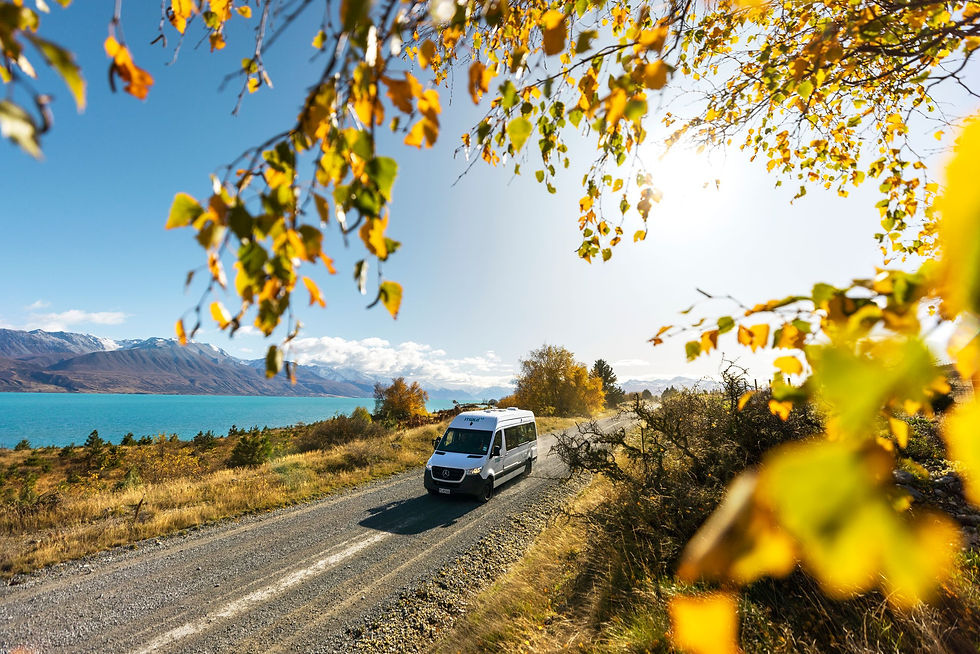 A van travels along a scenic country road, with a serene Lake Pukaki visible in the background.