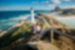 A couple ascends wooden stairs towards to view white Castlepoint Lighthouse with a green top on the rocky coastline.