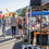 Thumbnail: People stroll through a bustling outdoor market on a sunny day. Various stalls display items like pottery and crafts.