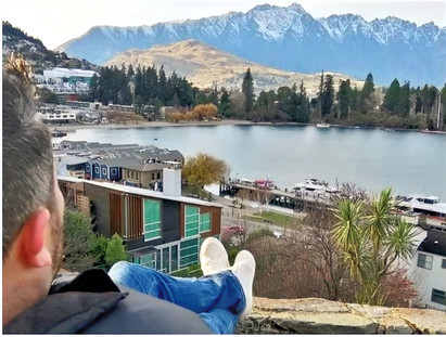 High-angle view of a person sitting atop a stone wall, overlooking a town nestled beside a lake.