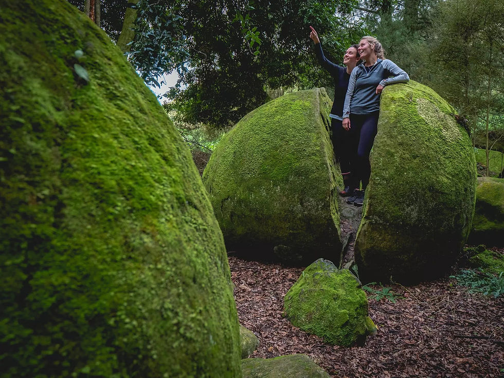 Thumbnail: Two people stand inside a large split boulder covered in green moss, capturing a selfie.