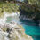 Thumbnail: A person wearing outdoor gear stands on rocky terrain beside a clear, turquoise river winding through Hokitika Gorge.
