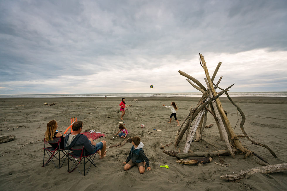 Thumbnail: A family enjoys a day at the beach as part of their Great Kiwi Trip. Two adults relax on chairs while two children play.