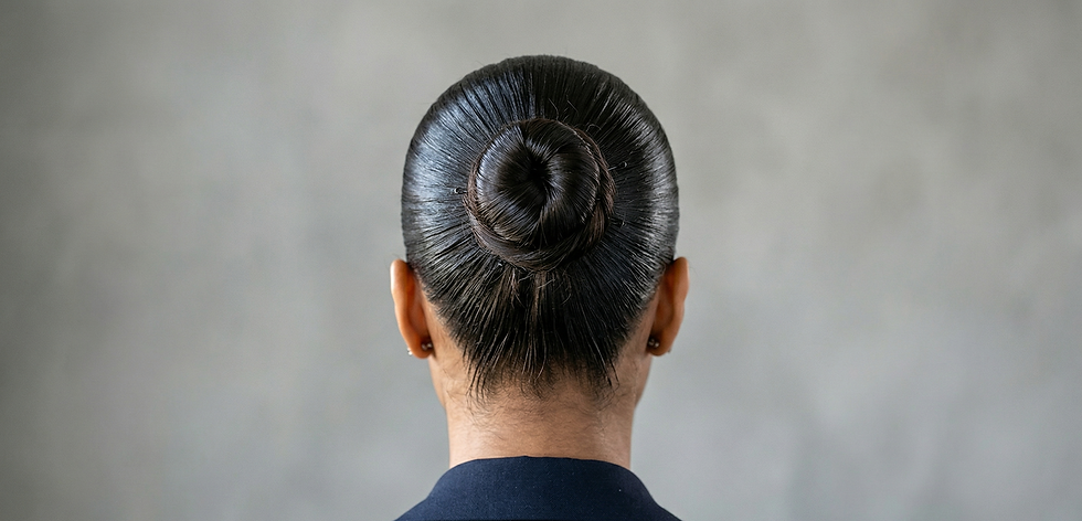Rear view of a person with neatly styled dark bun against a neutral gray background, wearing a dark top.