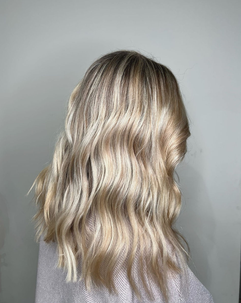 Wavy blonde hair, side view against a light gray background. Hair has subtle highlights and a soft, shiny texture.