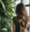 Rear picture of a sophisticated woman with long blowdried hair facing a indoor wall of plants