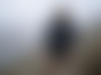 Homme courant sous la pluie sur un chemin de montagne rocheux et brumeux, vêtu d'un imperméable noir. Un autre coureur suit derrière.