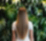 Rear picture of a sophisticated woman with long blowdried hair facing a indoor wall of plants