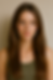 Woman with long brown hair and blue eyes in a green tank top stands against a plain beige background, exuding a calm expression.