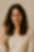 Woman with closed eyes and a serene smile, touching her hair. She's wearing a beige sweater against a tiled background. Calm mood.