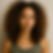 Woman with curly hair in a green tank top, standing against a neutral background, looking directly at the camera with a calm expression.