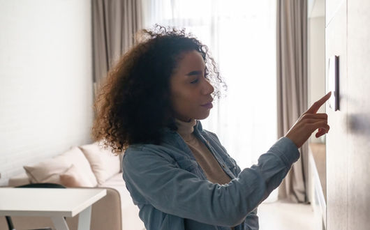 Woman using a smart home control panel on a wall, near a window.