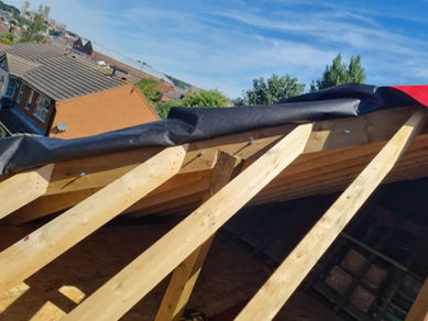 Construction scene with wooden roof beams extending from a building, partially covered by black ta