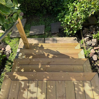 Wooden garden steps with metal railing, dappled sunlight creating leaf shadows