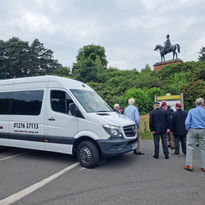 A white shuttle van parked near a group of people standing by a statue of a rider on a horse.