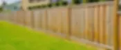 A long wooden fence with vertical planks runs along a manicured green lawn.