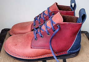 A pair of red and blue leather boots with blue laces sits on a wooden surface