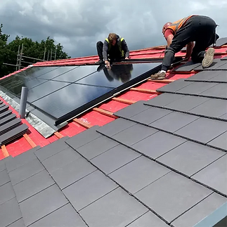 Two men installing solar panels on a sloped roof under a clear blue sky.