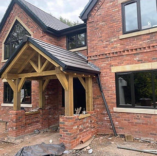 Red brick house under construction with black-framed windows and a wooden porch structure