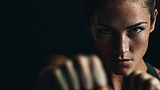 Femme au poing tendu, visage déterminé en gros plan sur fond noir, symbole de confiance et motivation.