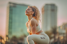 Femme athlétique souriante réalisant une fente avant avec des poids de musculation, devant un bâtiment flou, symbole de remise en forme et énergie.