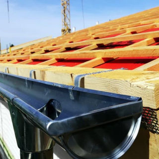 Pose de gouttière en zinc sur toiture en construction avec charpente bois et liteaux apparents