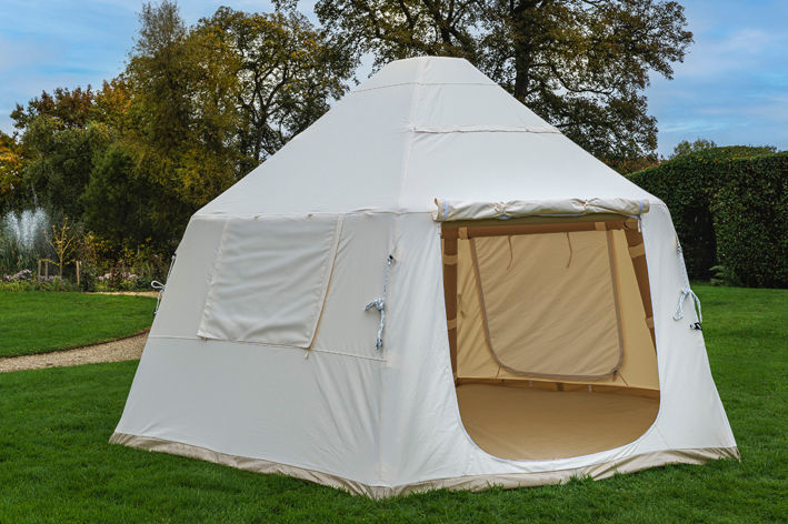 White bell tent on green grass, ready for camping in nature.