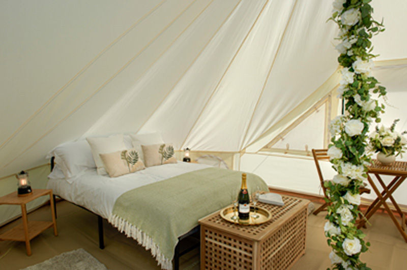 Cozy glamping tent interior with bed, flower garland, and champagne on the table.