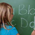 Schoolgirl writing letters on a blackboard.jpg