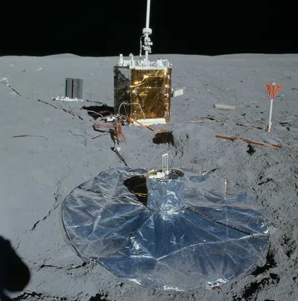 The Apollo 16 PSE is in the foreground, surrounded by its reflective thermal skirt. An orange-topped anchor for the Active Seismic Experiment geophone line is on the right, near the Central Station. Photo AS16-113-18347.