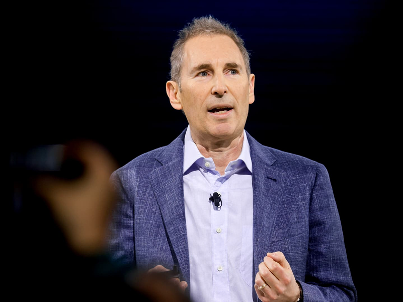 Amazon CEO Andy Jassy speaking on stage with a digital background, illustrating the $244 billion backlog and future AI chip roadmap.