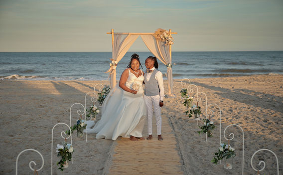 Two brides standing together on the beach in St. Croix, USVI with the ocean in the background during a same-sex destination beach wedding.